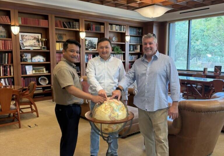 Three people in an office pointing to a country on a globe.