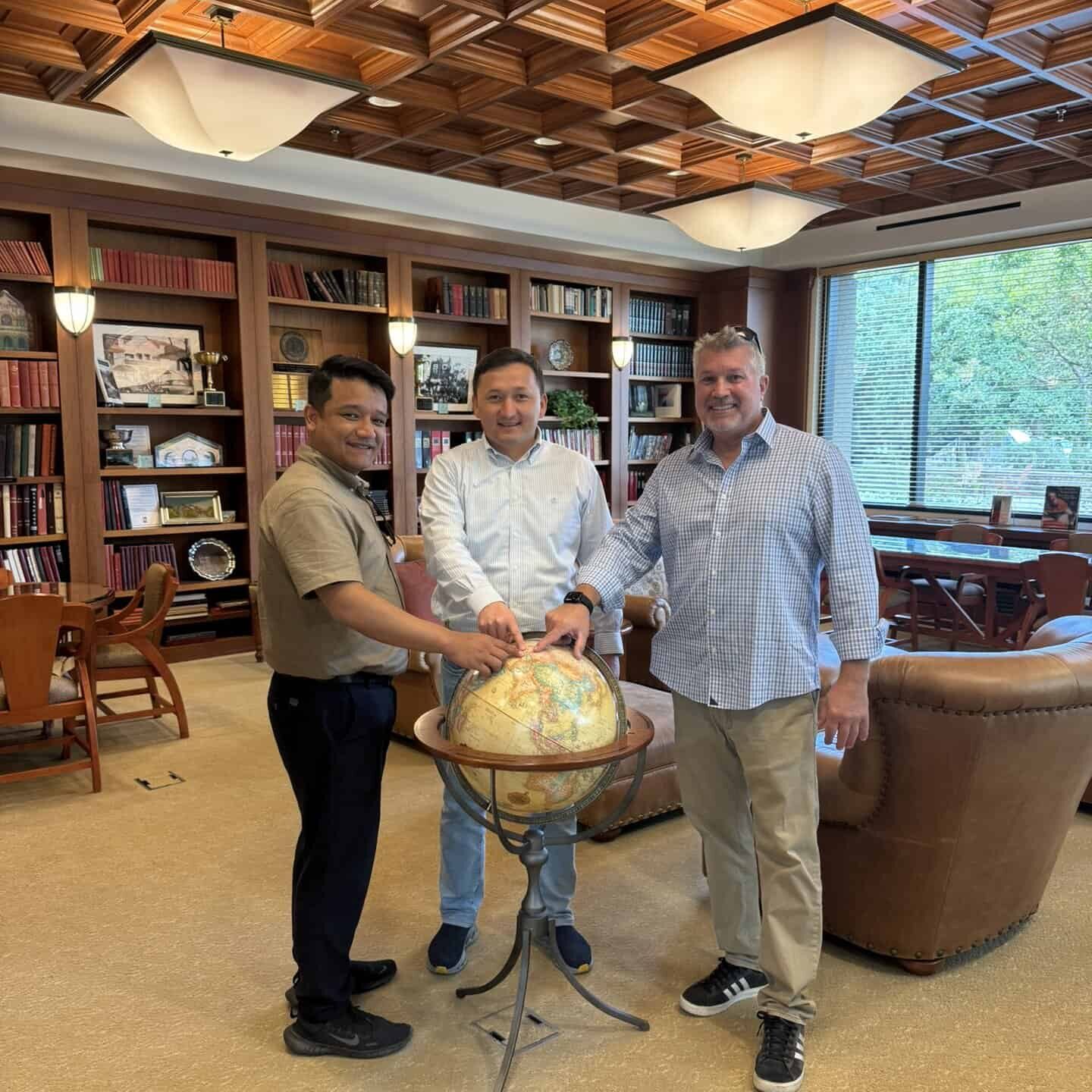 Three people in an office pointing to a country on a globe.